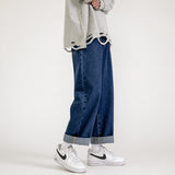 Grey torn shirt, wide blue jeans, white Nike shoes, minimalist white background.