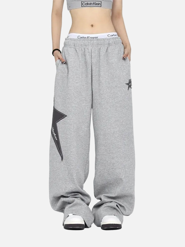 Grey Calvin Klein crop top, oversized grey sweatpants with star, white sneakers, white background.