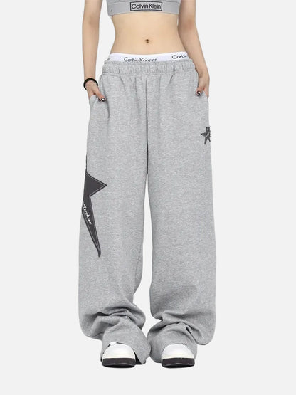 Grey Calvin Klein crop top, oversized grey sweatpants with star, white sneakers, white background.