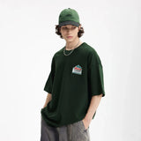 Moel wearing the green The Unity T-Shirt in a gray background
