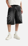 Model wearing the black Denim Patchwork Shorts in a gray background 