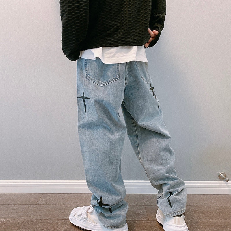 Black textured sweater, white shirt, light blue jeans with crosses, white sneakers, wooden background.