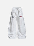 White wide-leg nylon track pants with contrast black piping, a fold-over waistband, and retro football crest graphics on the thighs.