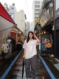 A model wearing an oversized pink and white mesh football jersey with a central number 7, standing in a city alleyway.