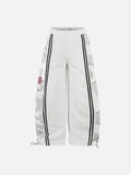 Light grey wide-leg joggers featuring camo side panels, black track stripes, red graphic prints, and adjustable toggle hems.