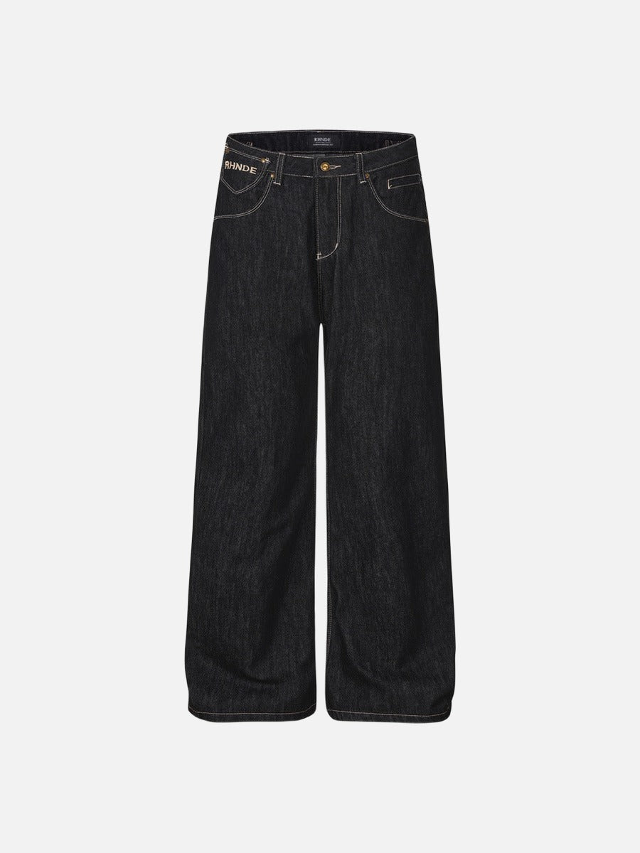 Dark wash wide-leg streetwear jeans with contrast stitching, gold-tone hardware, and script letter embroidery on the back pockets.